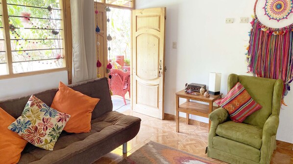 A living room with a sofa, a green armchair, a wooden table, and a door leading outside.