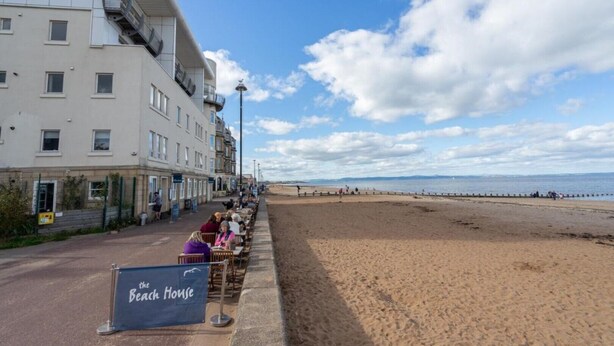 A seaside hotel with a terrace overlooking the beach, a sign for 'The Beach House', and a row of buildings with balconies. - Immaculate Family sized holiday home located 10mins from beachfront! (Edinburgh)