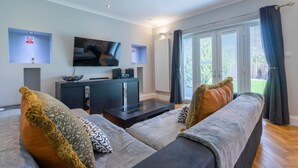 A modern living room with a flat-screen TV, a dark entertainment unit, and a sofa with patterned cushions. - Immaculate Family sized holiday home located 10mins from beachfront! (Edinburgh)