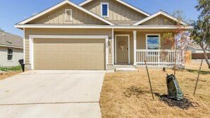 A two-story house with a beige garage door, a front porch with a white railing, and a small window above the door. - Spacious, NEW Home with Gorgeous Edison Patio (San Antonio)