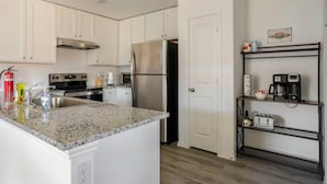 A kitchen with white cabinets, a granite countertop, stainless steel appliances, and a black metal shelf with a coffee maker and toaster. - Spacious, NEW Home with Gorgeous Edison Patio (San Antonio)