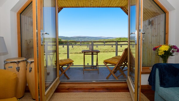 Une pièce dotée d’un plafond en bois, d’une porte vitrée donnant sur un espace extérieur avec une table et des chaises, et offrant une vue sur la campagne.