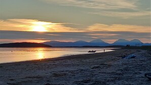 Une plage avec un bateau sur l’eau, des montagnes en arrière-plan et un ciel dégagé.