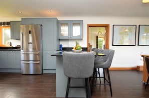 A modern kitchen with grey cabinets, a stainless steel refrigerator, and a dining area with a bar stool and a table.