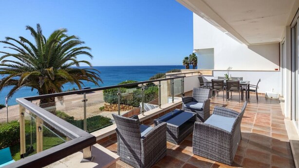 Un balcon doté de meubles en osier, d’une rambarde en verre et offrant une vue sur la mer.