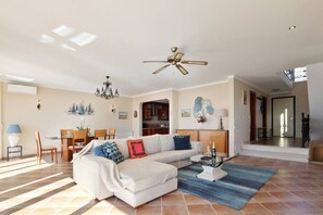 A spacious living room with a sectional sofa, a dining area with a table and chairs, a kitchen in the background, and a ceiling fan. - Casa del Mar - An Amazing Villa w/ Sea View & Pool (Luz)