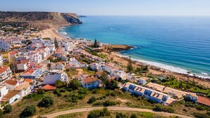 Une ville côtière avec des bâtiments qui bordent la plage, une vue dégagée sur la mer et un paysage vallonné en arrière-plan.