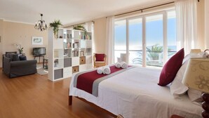 Une chambre d’hôtel avec un grand lit, une bibliothèque, un bureau et une vue sur l’océan.
