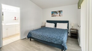 A bedroom with a bed, a nightstand, a lamp, a painting, and a view of a beach. - Huge screened patio that overlooks Lake Buck, near famous attractions!! (Kissimmee)