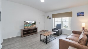 A modern living room with a flat-screen TV, a wooden coffee table, a grey sofa, and a window with a view of the outside. - Huge screened patio that overlooks Lake Buck, near famous attractions!! (Kissimmee)
