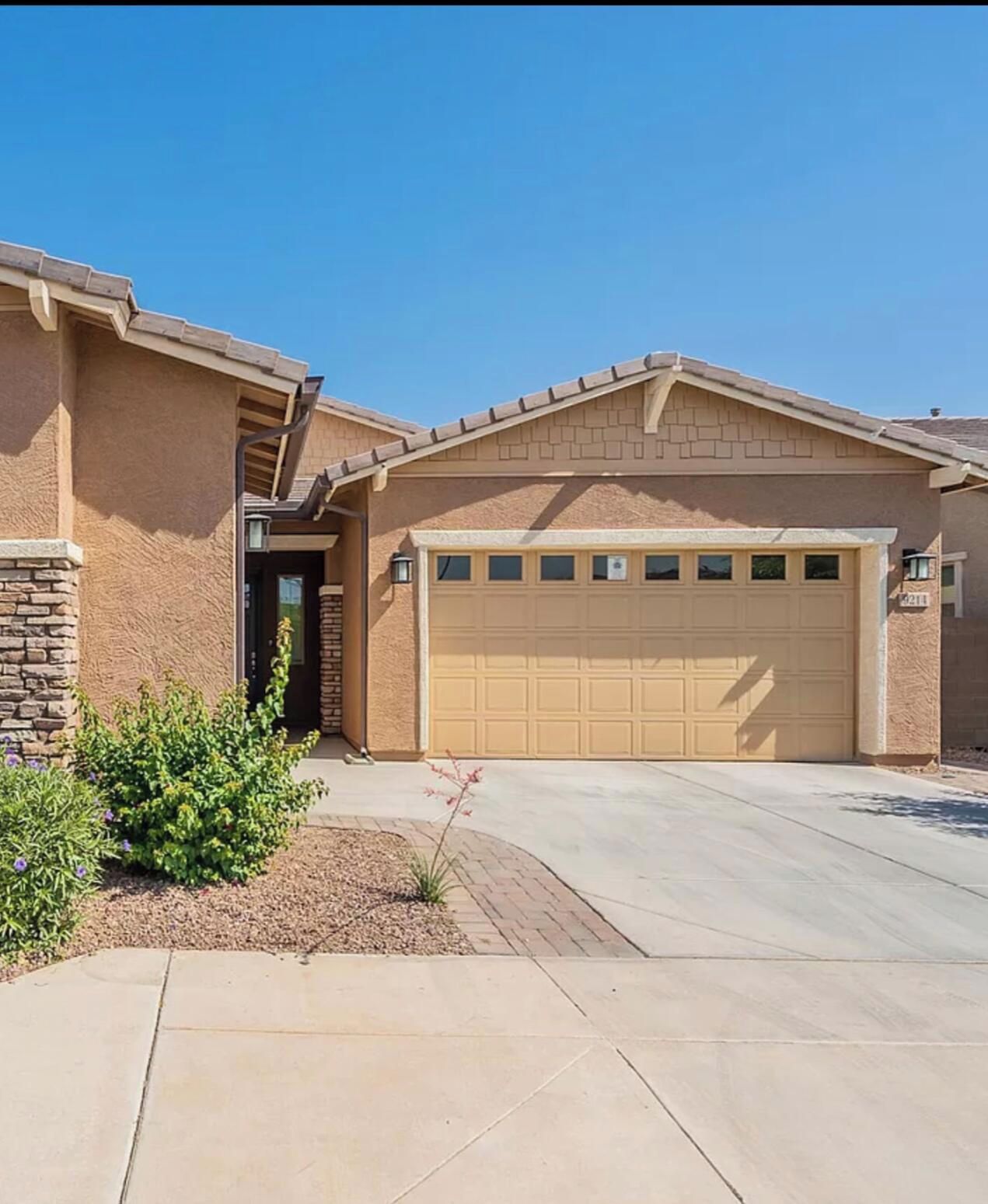 A single-story house with a garage, a stone foundation, and a landscaped front yard.