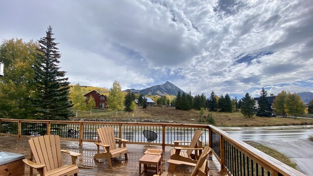 A wooden deck with Adirondack chairs, a stone wall, and a view of a river and mountains. - Mountain Vintage Vacation Home! Conveniently in Mt CB, easy access to trails! (Crested Butte)