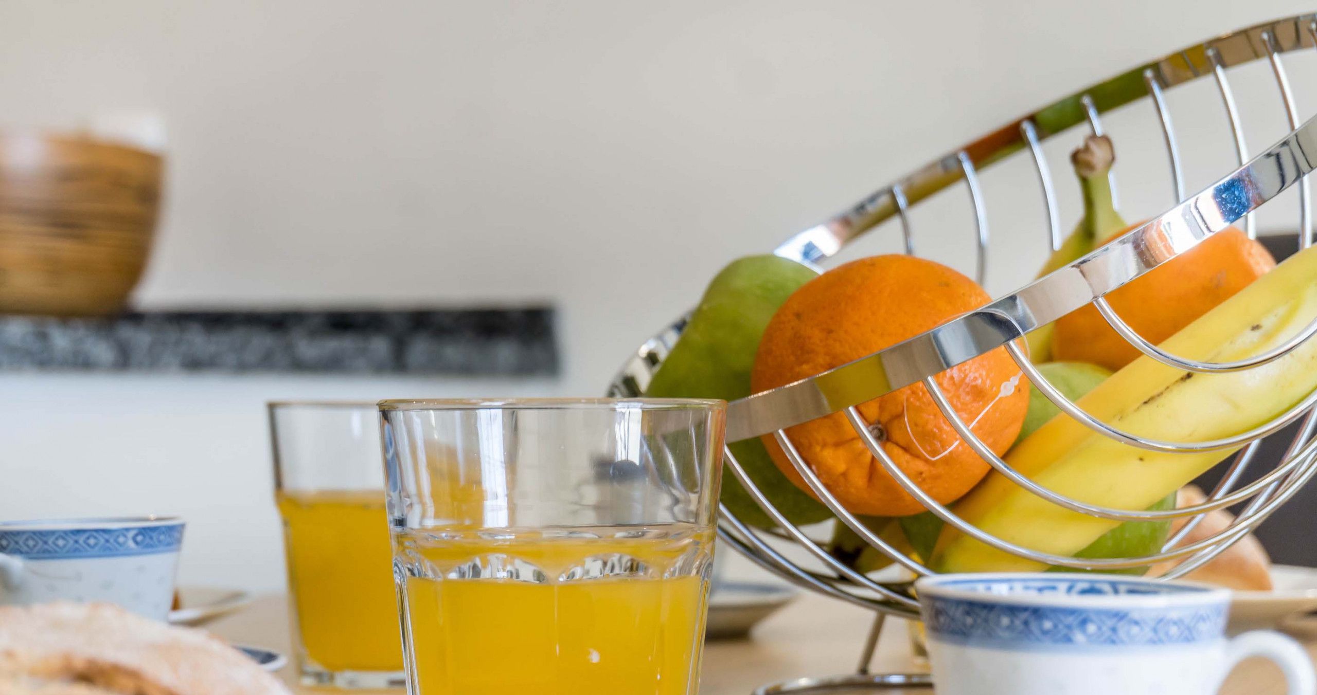 A breakfast setting with a fruit bowl, a glass of orange juice, and a cup on a table.