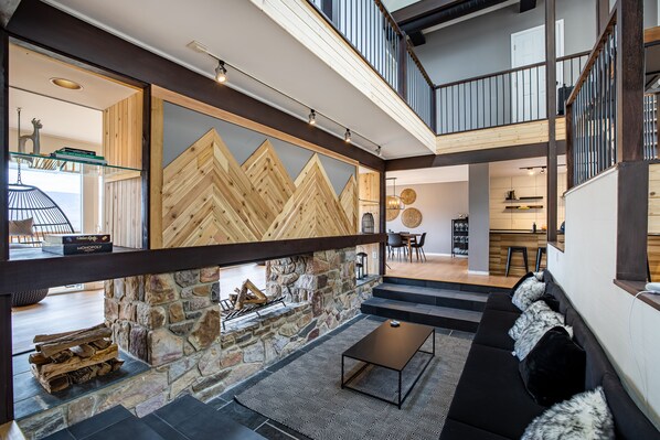Un intérieur moderne avec une cheminée en pierre, un canapé noir et un coin repas.