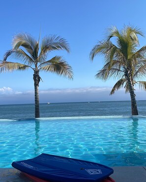 Une piscine à débordement à l’eau d’un bleu cristallin, bordée de palmiers et offrant une vue sur l’océan.