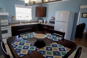 A kitchen with a stove, sink, microwave, and refrigerator. There is a dining table with a bowl and placemats. - Whistler's View (Twillingate)