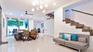 A spacious living area with a modern staircase, a dining set, and a sofa with cushions. - The Castle II - Modern Villa with Private Pool at a Safe Gated Community (Cancún)