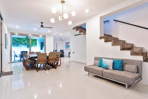A spacious living area with a modern staircase, a dining set, and a sofa with cushions.