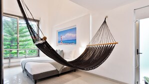 Un dormitorio moderno con una hamaca, un ventanal con vistas a la vegetación y un cuadro de un faro en la pared.