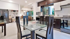 Una cocina moderna con armarios oscuros, una mesa de comedor de vidrio y vistas al exterior.
