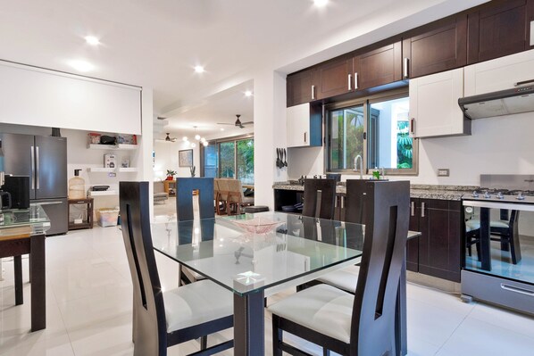 A modern kitchen with dark cabinets, a glass dining table, and a view of the outdoors. - The Castle II - Modern Villa with Private Pool at a Safe Gated Community (Cancún)
