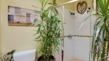 A bathroom with a toilet, a shower, and a potted plant.