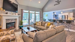 A modern living room with a fireplace, a large flat-screen TV, and a dining area with bar stools.