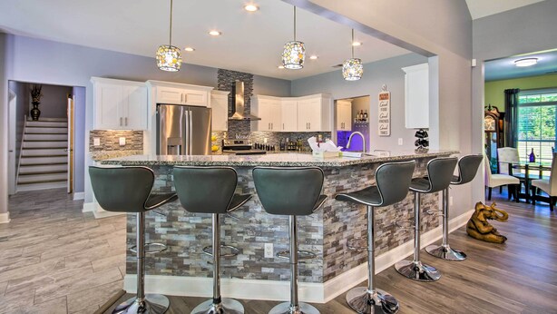 A modern kitchen with a central island, bar stools, pendant lighting, and a stainless steel refrigerator.