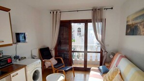 Een gezellige woonkamer met een bank, een stoel, een kleine tafel, een wasmachine en een televisie op een plank.