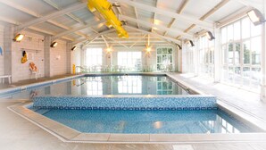 Une piscine intérieure aux carreaux bleu clair, avec un toboggan jaune pour les sauveteurs et de grandes fenêtres laissant entrer la lumière naturelle.