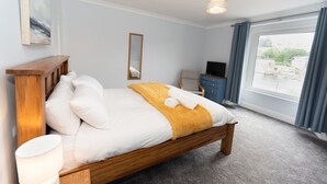 Une chambre d’hôtel avec un lit en bois, une lampe de chevet, un téléviseur à écran plat, une fenêtre avec des rideaux et une vue sur la ville.