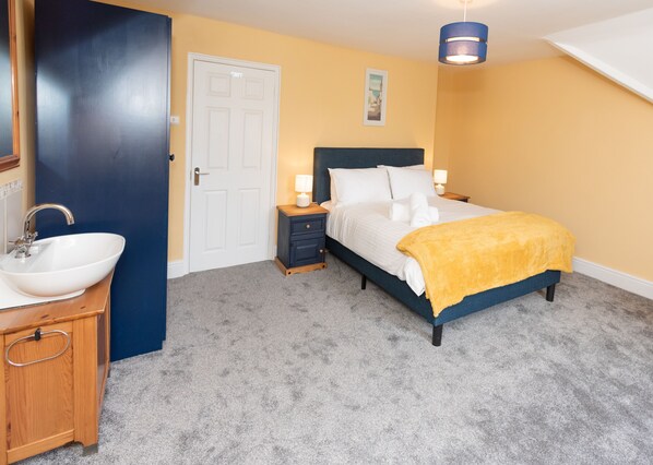 A bedroom with a bed, bedside tables, a nightstand, a sink, and a door.