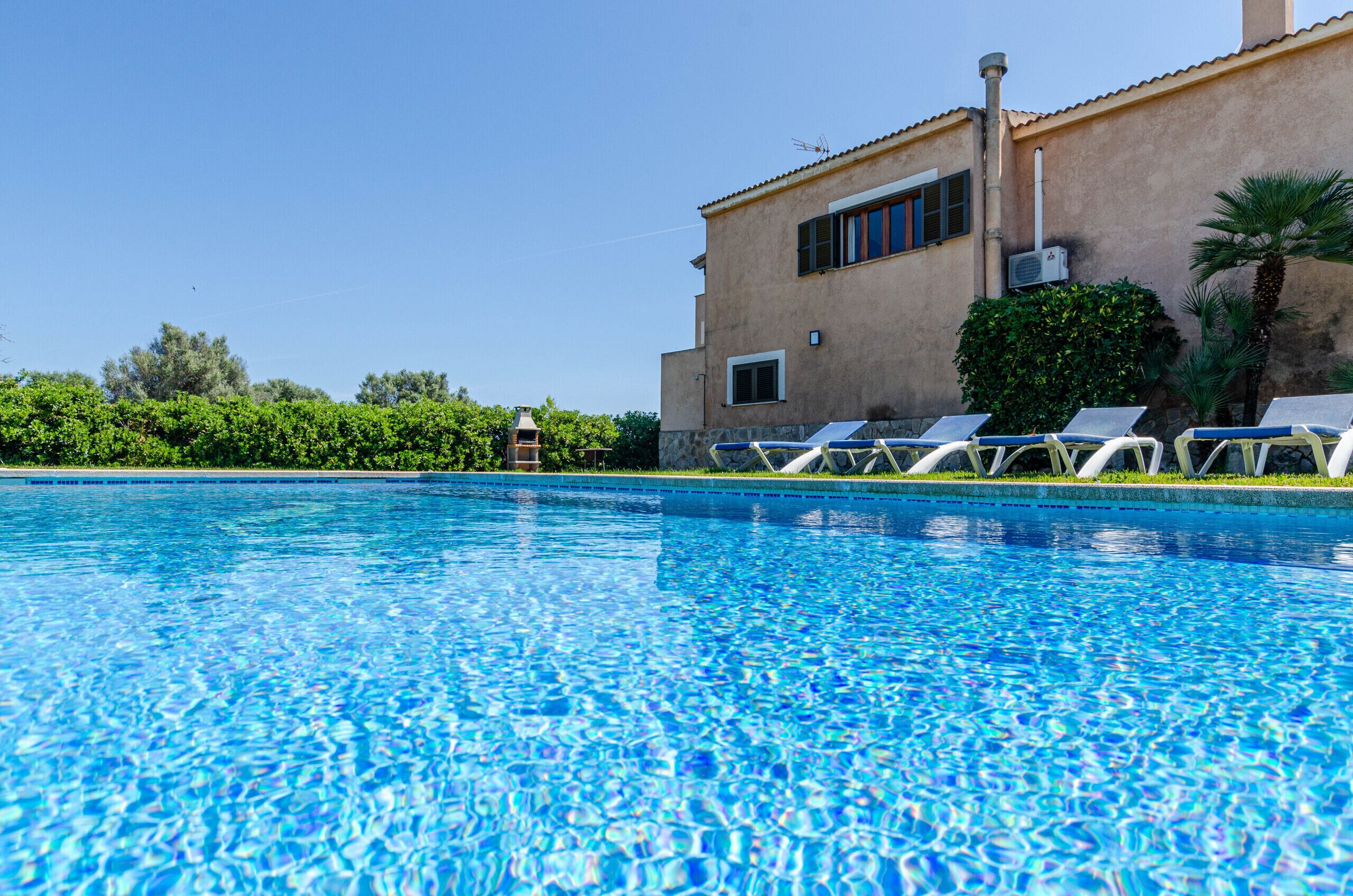 Una piscina con sillas de descanso, un edificio con techo de tejas y follaje al fondo.