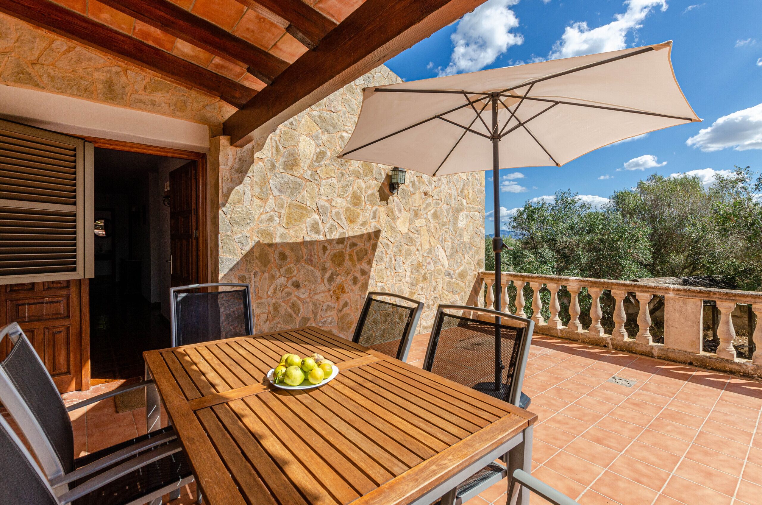 A wooden table with chairs and a plate of fruit, a stone wall, and an umbrella on a patio.