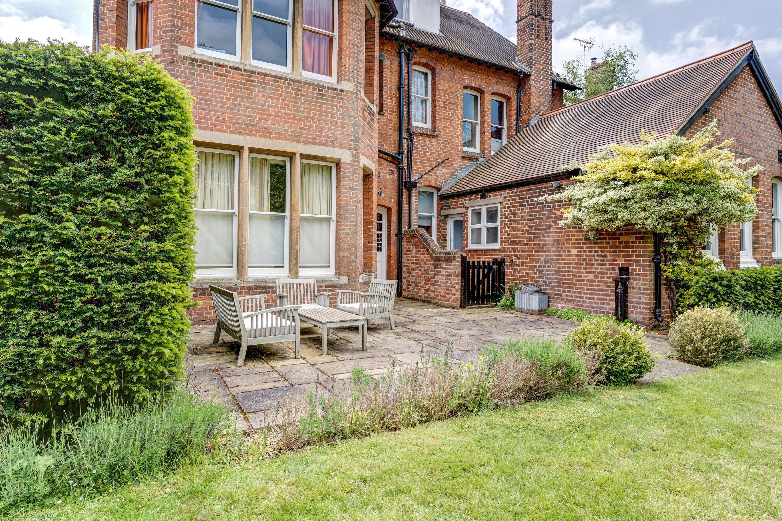 A brick house with a patio, a hedge, and a small garden.