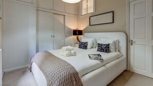 Quarto bem arrumado com cama, mesas de cabeceira, abajur e um quadro na parede.