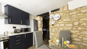 Une cuisine moderne avec des meubles de couleur sombre, un four à micro-ondes et un grille-pain. On y trouve une table de petit-déjeuner avec des assiettes, un croissant et un verre de jus d’orange.