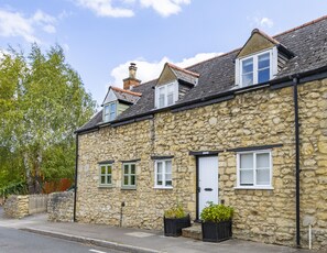 A stone building with multiple windows and a door, surrounded by greenery. - Bushnells Cottage | Oxfordshire Holiday Let | 2 Beds & Sleeps 3 (Oxford)