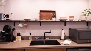 Et køkken med kaffemaskine, mikroovn og et hyldes med service samt et skilt med teksten "LET'S EAT".