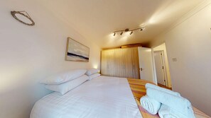 A bedroom with a bed, pillows, a painting, a wardrobe, and a set of towels.