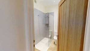 Un baño moderno con ducha de vidrio, azulejos blancos y puerta de madera.