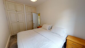 Een slaapkamer met een bed, een houten nachtkastje, een kledingkast en een spiegel.