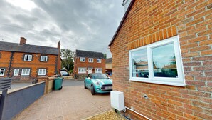 Une rue résidentielle bordée de maisons en briques, avec une voiture garée et une boîte électrique visible sur le côté d’une maison.