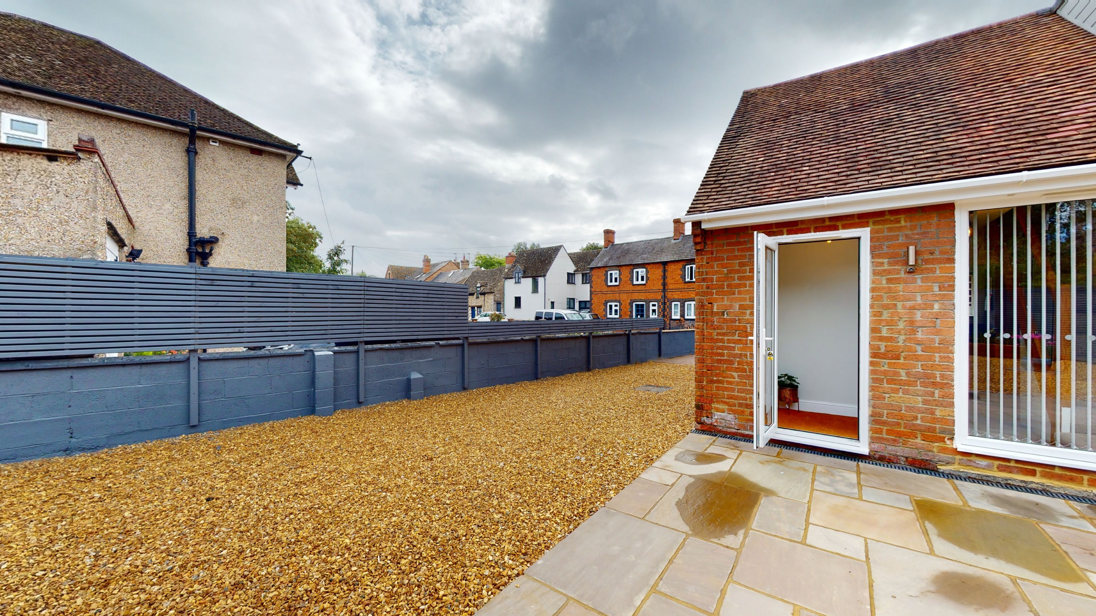 A residential property with a gravel driveway, a metal fence, and a brick house with a glass door.