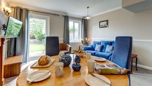 Una sala de estar con una mesa de comedor preparada para el desayuno, un sofá azul y un televisor montado en la pared.