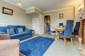 Ein Wohnzimmer mit einem blauen Sofa, einem Couchtisch und einem Essbereich mit blauen Stühlen.