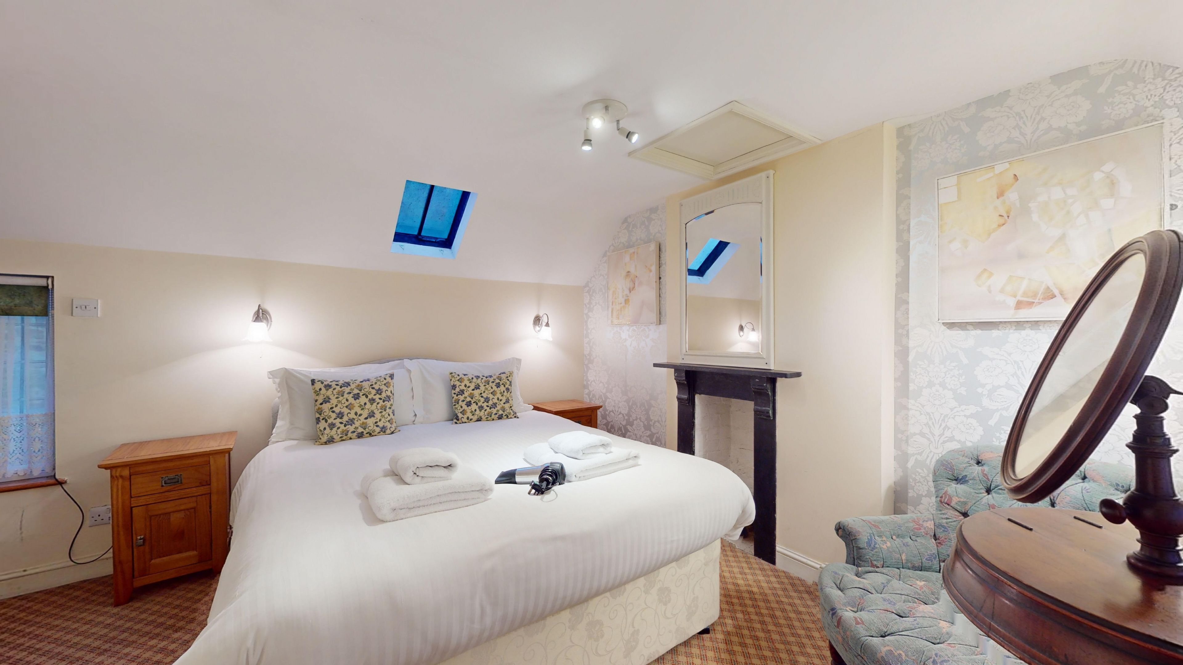 A neatly arranged bedroom with a bed, bedside tables, a dresser, a mirror, and a wall-mounted light fixture.