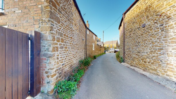 A narrow alleyway flanked by stone buildings with a wooden fence on one side.