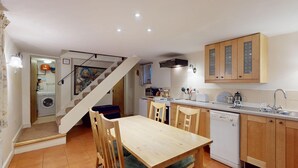 A compact kitchen with wooden cabinets, a dining table, and a staircase leading to a laundry area.