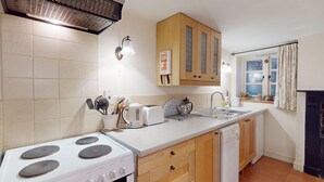 A compact kitchen with a stove, toaster, sink, and wooden cabinets.